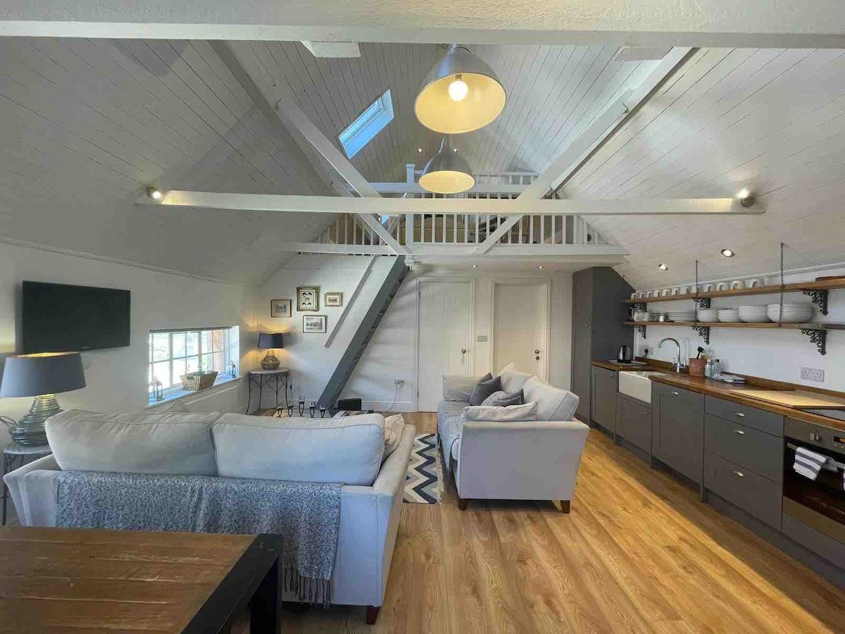 A spacious living area with a staircase leading to a loft, a kitchen with wooden countertops, and a dining area with a table and chairs.