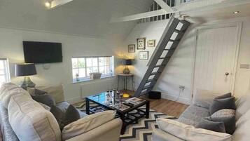 A spacious living room with a high ceiling, a staircase, and a television mounted on the wall.