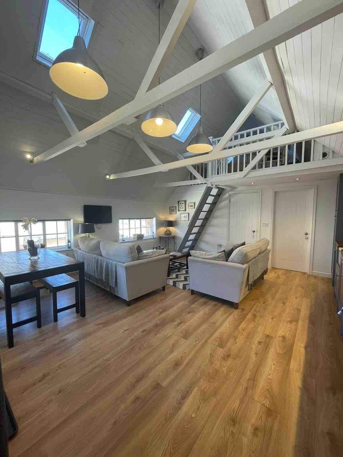 A spacious living area with a high ceiling, wooden flooring, and a staircase leading to an upper level.
