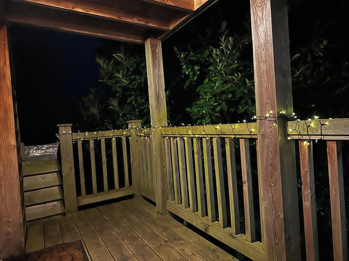 Eine Holzterrasse mit Geländer, einer Treppe und Lichterketten.