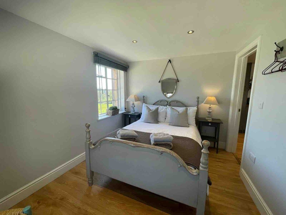 A bedroom with a bed, bedside tables, a hanging mirror, and a window.