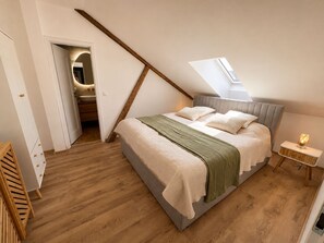 A bedroom with a sloped ceiling, a bed with pillows, a bedside table with a lamp, and a wooden floor.