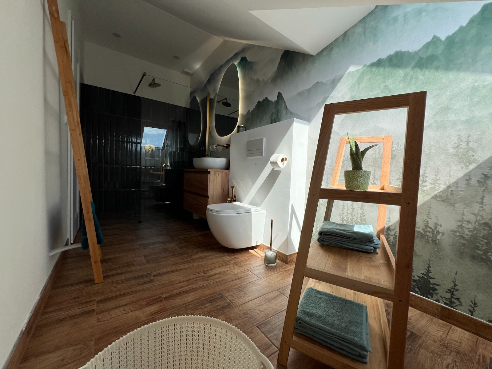 A modern bathroom with a wooden floor, a white toilet, a sink, and a mirror. There is a window with a view of trees and a mountain.