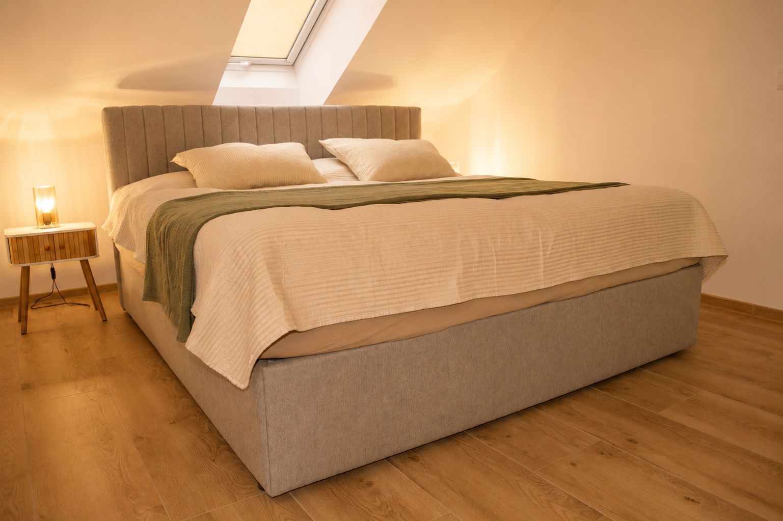 Een slaapkamer met een bed, een nachtkastje met een lamp en een dakraam.
