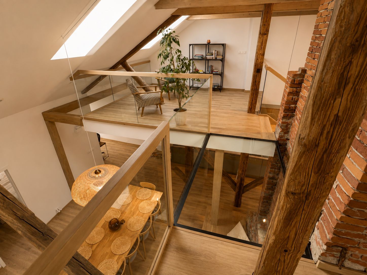 Een meerlaags interieur met een eethoek beneden, een trap en een vide met een boekenkast en planten.