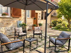An outdoor seating area with chairs and tables, a covered umbrella, and a stone wall.