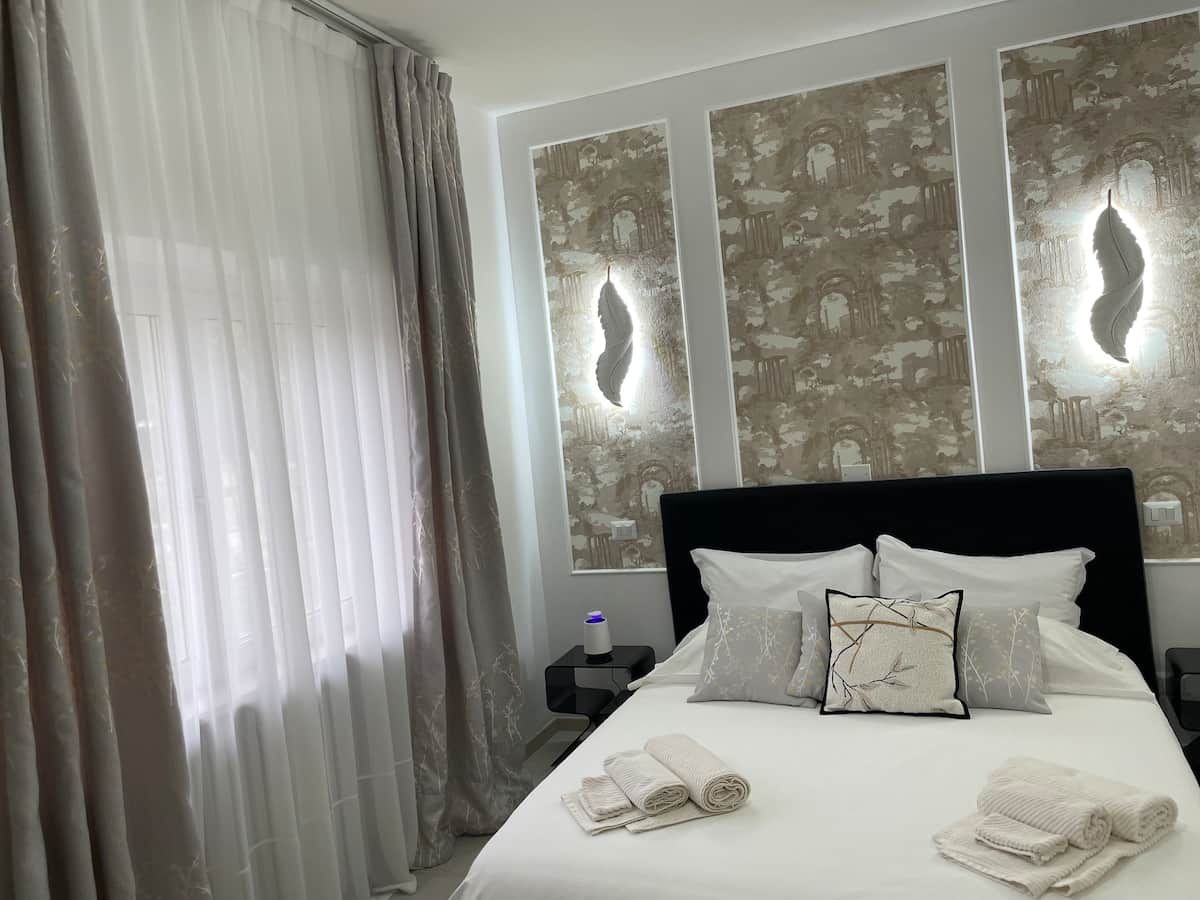 Una camera d'albergo con un letto, tende, un comodino e decorazioni a parete.