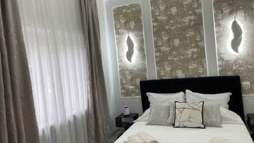 Una camera d'albergo con un letto, tende, un comodino e decorazioni a parete.