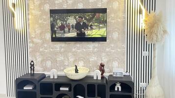 Een moderne woonkamer met een flatscreen televisie aan de muur, een zwarte entertainmentkast met planken, een decoratieve vaas en behang met een patroon.
