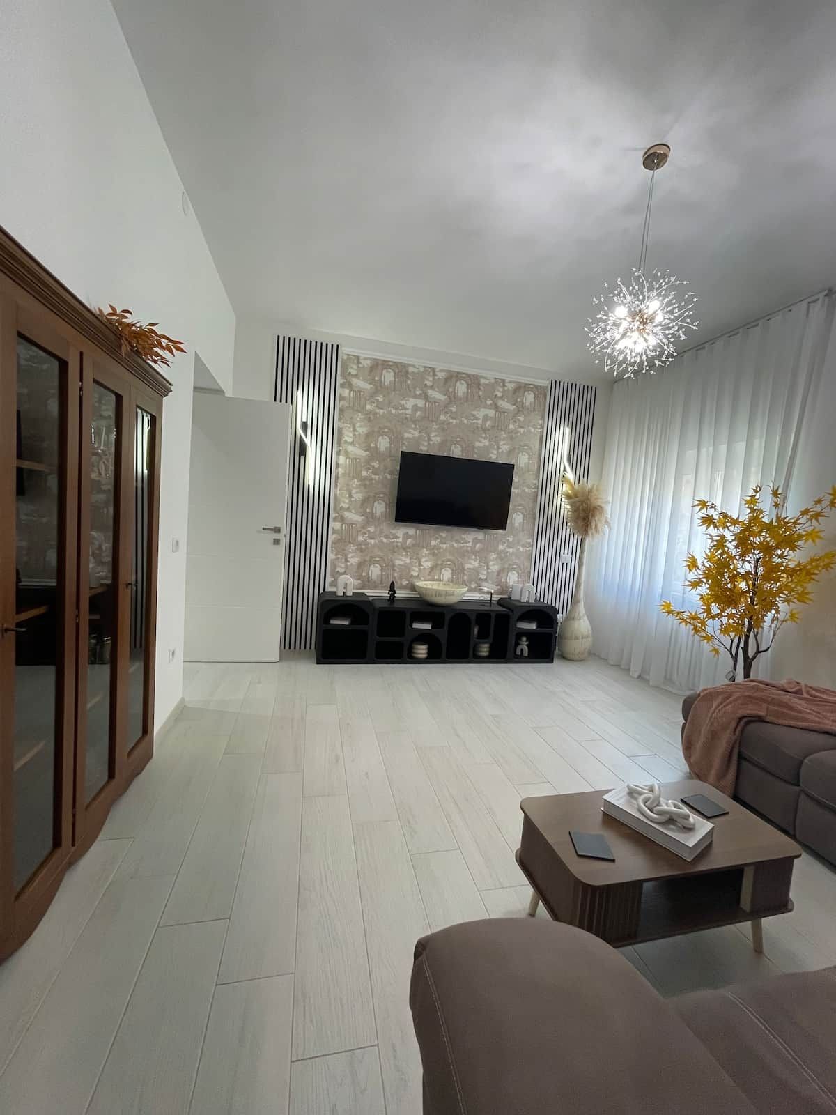 Ein modernes Wohnzimmer mit Flachbildfernseher, einer Wanddekoration, einer Couch, einem Couchtisch und einer Pendelleuchte.