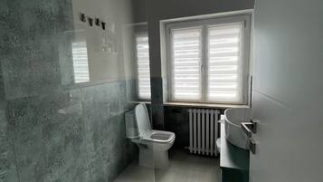 Ein modernes Badezimmer mit Toilette, einer Duschkabine aus Glas und einem Fenster mit Jalousien.