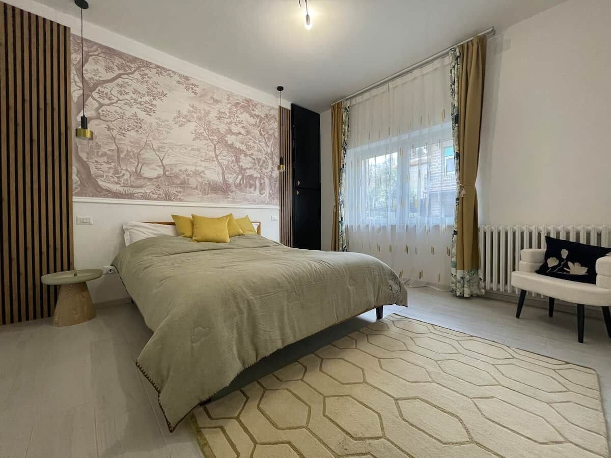 Une chambre moderne avec un grand lit, une table de chevet ronde, un fauteuil blanc et une fresque murale.