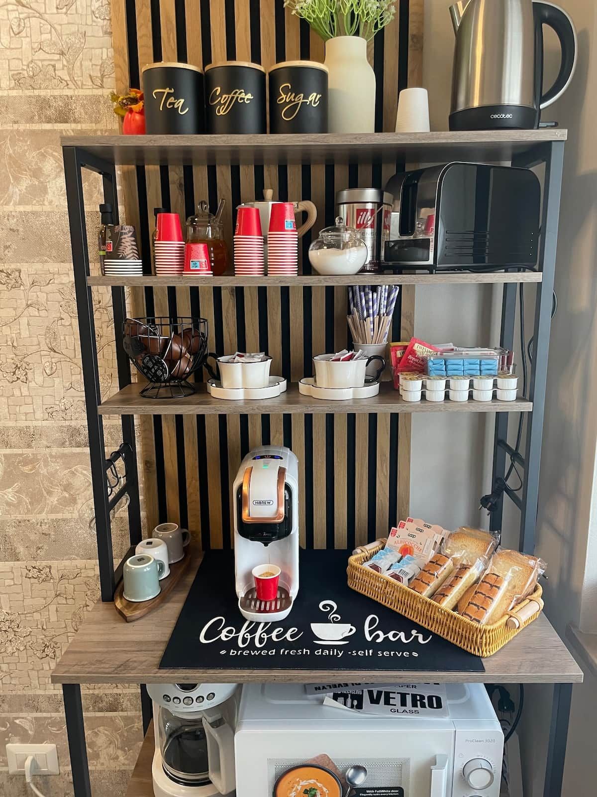 Un angolo caffetteria con macchina per caffè, tazze, zucchero e contenitori per tè.