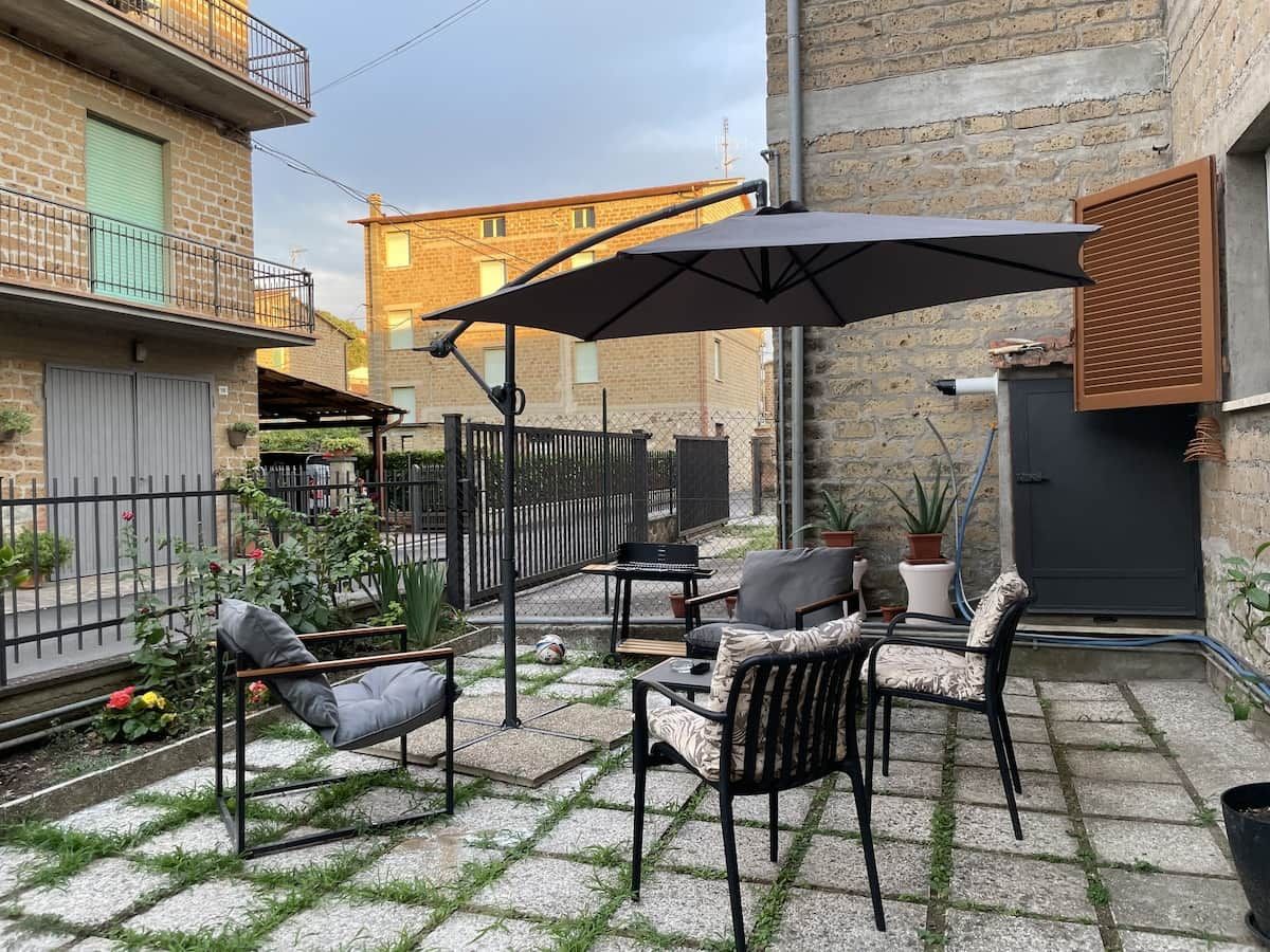 Eine Terrasse im Freien mit Tisch und Stühlen, einem großen Sonnenschirm und Kübelpflanzen.