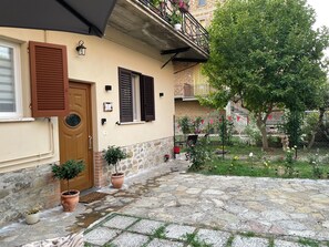 A stone-paved courtyard with potted plants, a wooden door, and a balcony with railings.