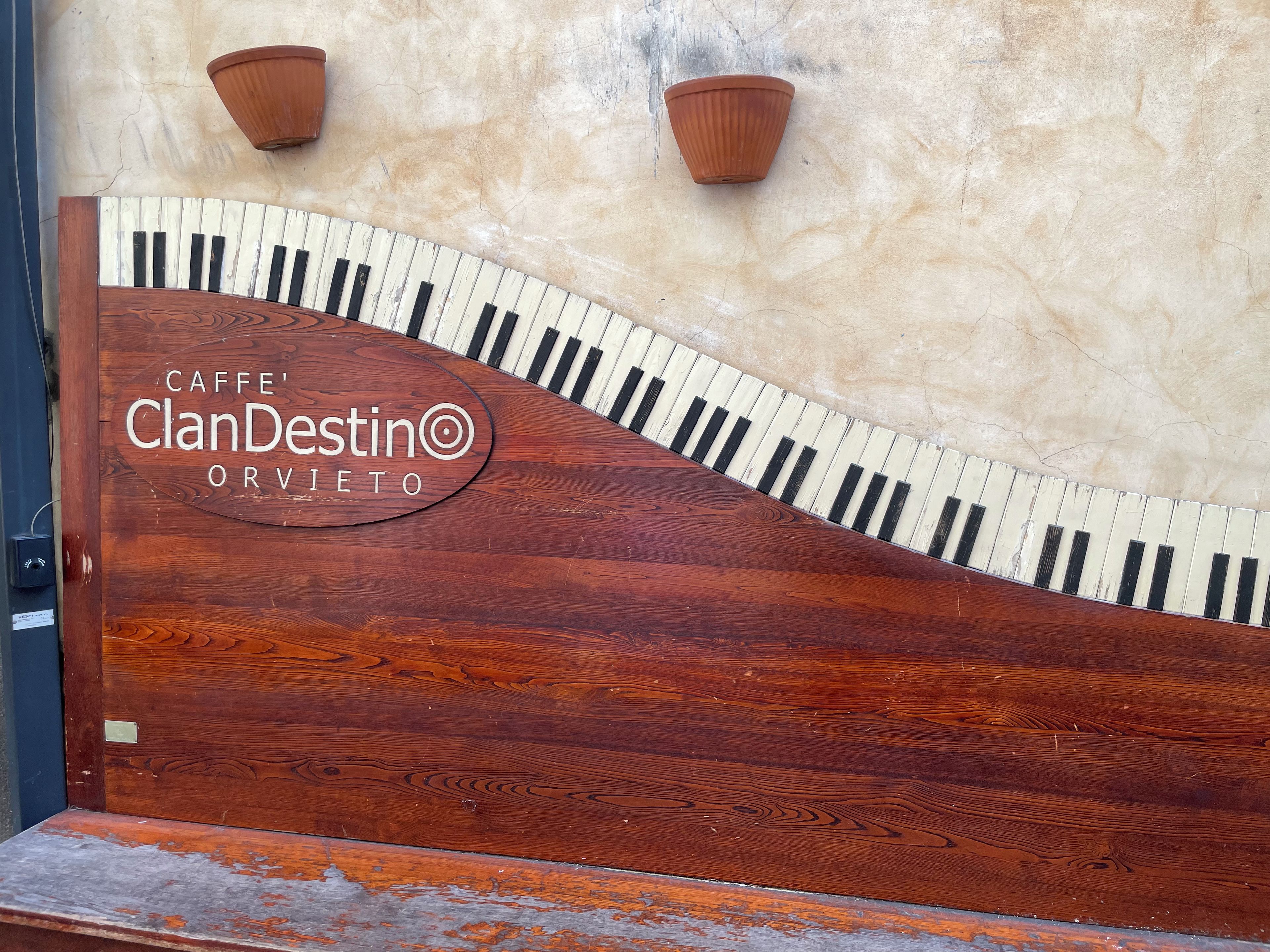 A wooden piano with a logo that reads 'CAFFE' ClanDestino ORVETO' on a wall.