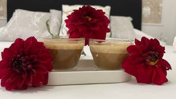 Duas taças com bebida castanha sobre um tabuleiro branco com flores vermelhas.