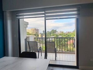 Ein Zimmer mit einer großen Schiebeglastür, die auf einen Balkon mit Blick auf Gebäude und Bäume führt.