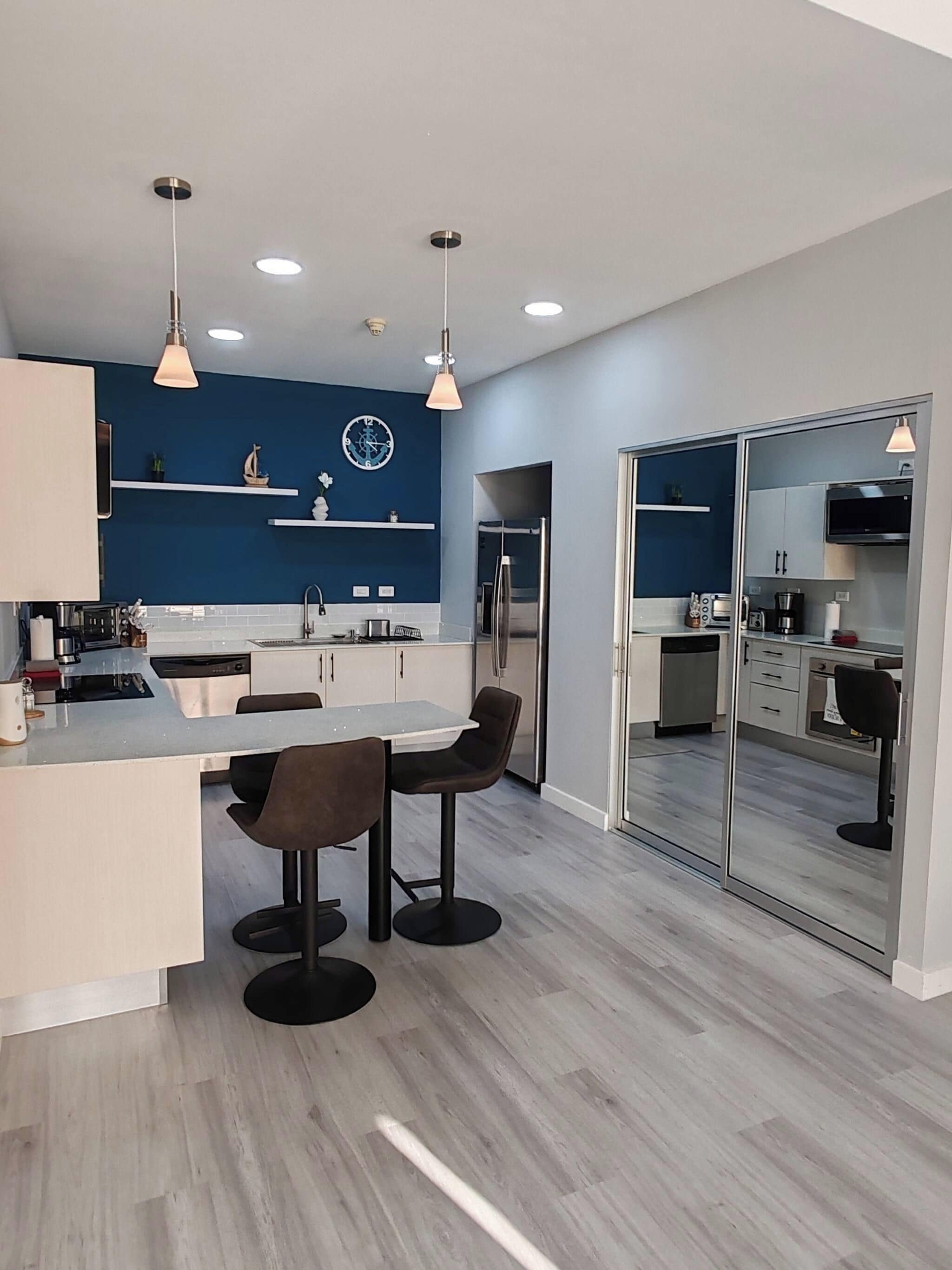 Una cucina moderna con isola centrale, illuminazione a sospensione e un ampio specchio.