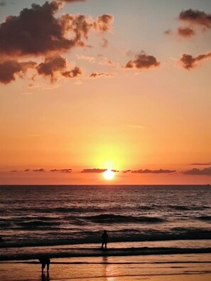 Ein Sonnenuntergang über dem Meer mit einer Person, die am Strand steht.