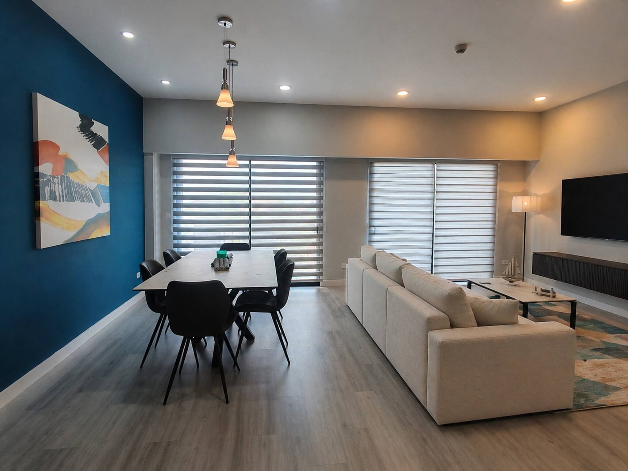 A modern living room with a dining area, a sofa, a TV, and a painting on the wall.