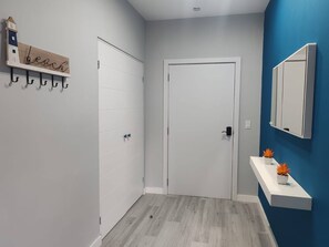 A hallway with a white door, a wooden sign with 'beach' written on it, a white wall-mounted mirror, and a blue accent wall. - Modern 3BR Condo in Jacobay - Walk to the Beach 2blocks (Jacó)