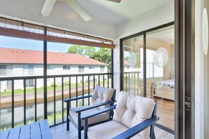 A balcony with a sofa and a table, a bedroom with a bed and a wall decoration, and a view of a building with a red roof. - 15 Min from AMI Beaches, Pickleball, Basketball. Free WIFI (Bradenton)