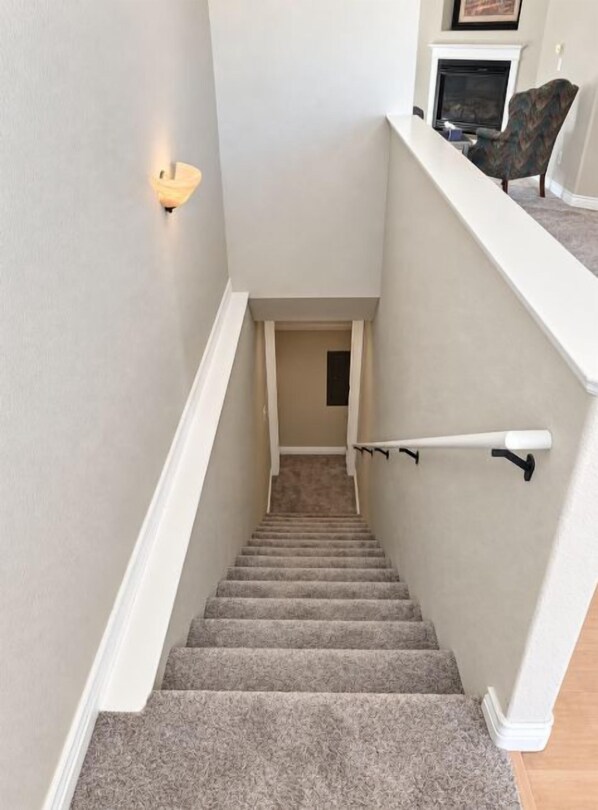 A carpeted staircase with a handrail, a light fixture on the wall, and a chair on the landing.