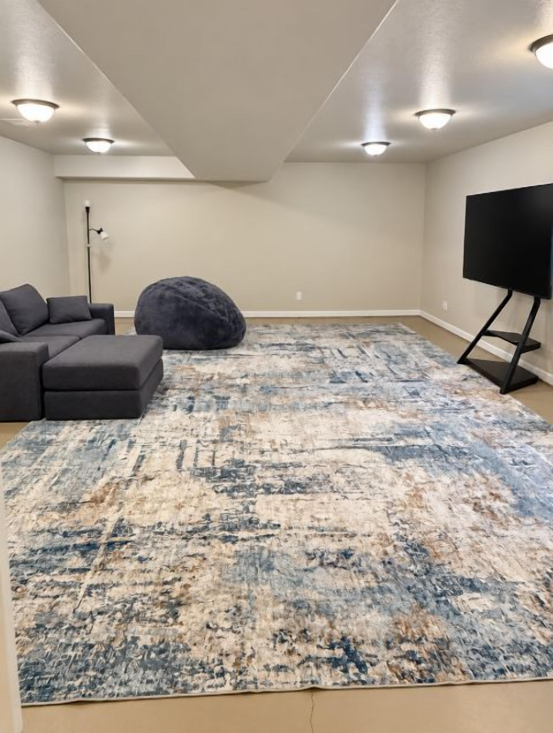 A living room with a sectional sofa, a large rug, a bean bag, and a TV on a stand.