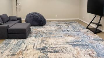 A living room with a sectional sofa, a large rug, a bean bag, and a TV on a stand.