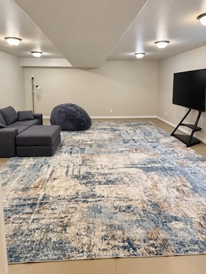 A living room with a sectional sofa, a large rug, a bean bag, and a TV on a stand. - Settle in for fall in this spacious 3BR, 3BA Casper townhome! A private bath for every bedroom, two living areas, a full kitchen, washer/dryer, and a fenced backyard make it perfect for hunting trips, work crews, and holiday visits with family. (Casper)