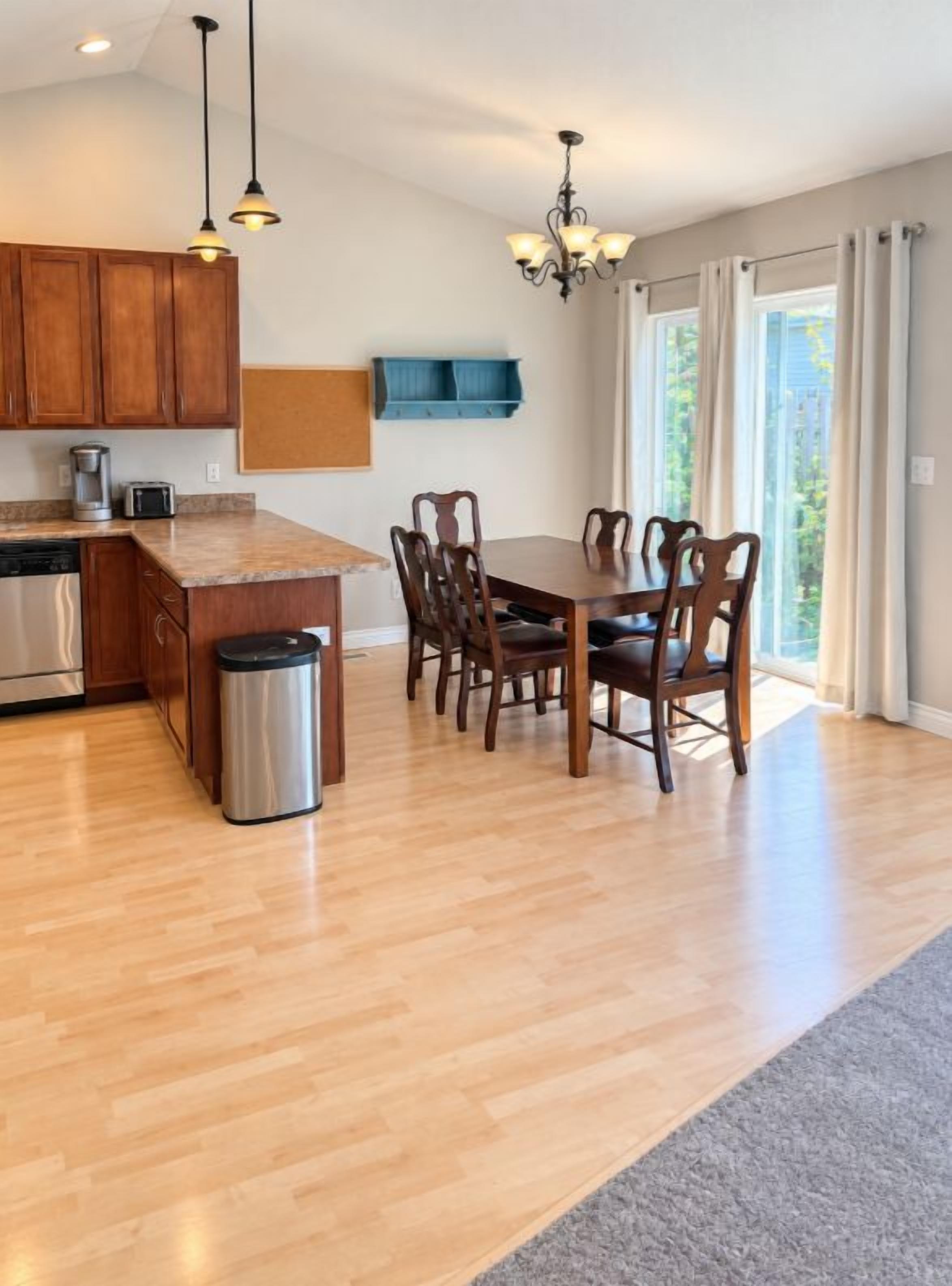 A modern kitchen with wooden cabinets, a granite countertop, and a dining area with a table and chairs.