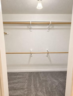 A walk-in closet with a wooden rod and hooks, a light fixture, and a carpeted floor. - Settle in for fall in this spacious 3BR, 3BA Casper townhome! A private bath for every bedroom, two living areas, a full kitchen, washer/dryer, and a fenced backyard make it perfect for hunting trips, work crews, and holiday visits with family. (Casper)