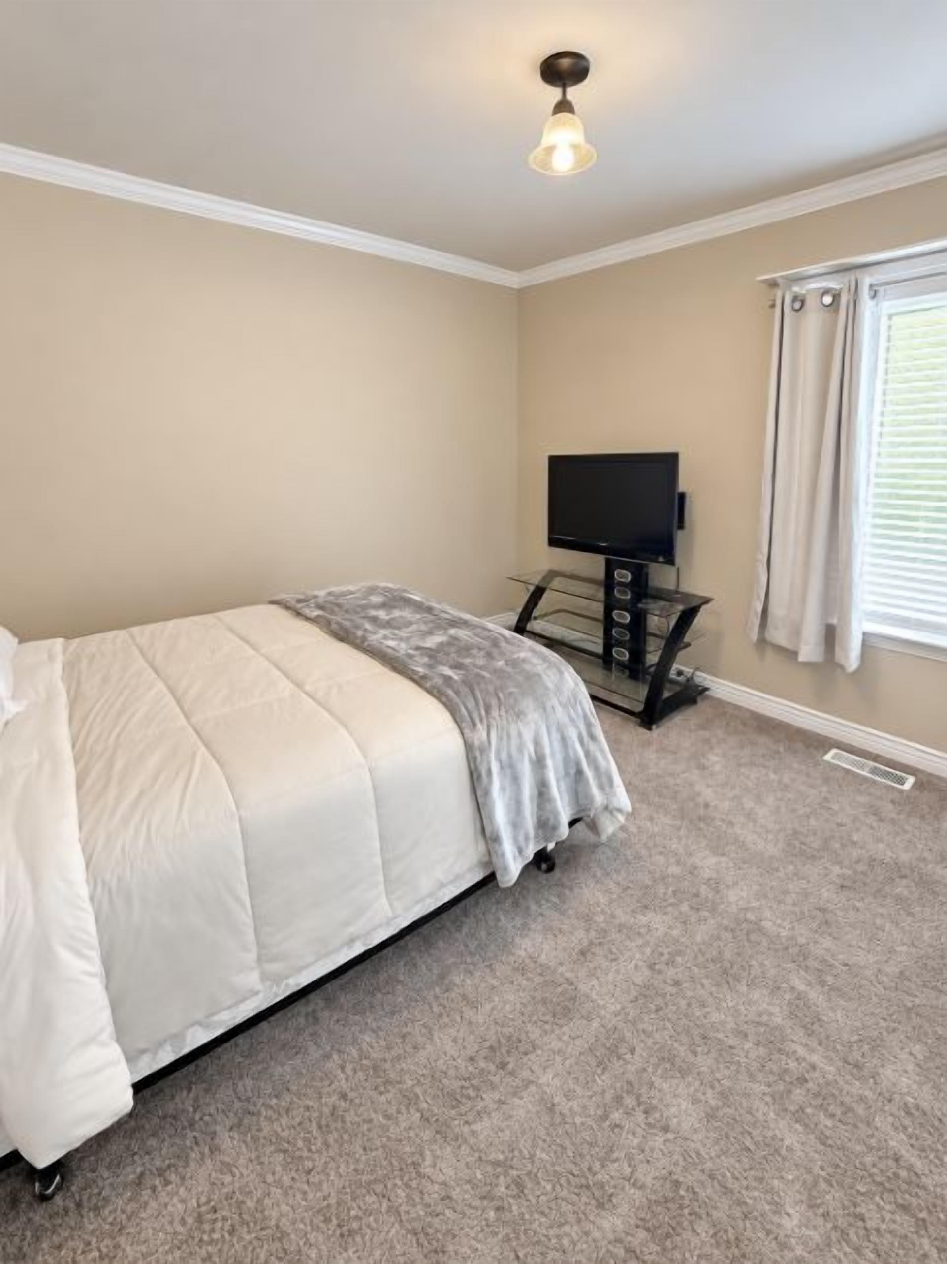 A bedroom with a bed, a television on a stand, and a window with curtains.
