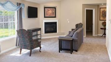 A spacious living room with a fireplace, a ceiling fan, and a large window.
