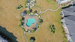 An aerial view of a property with a swimming pool surrounded by lounge chairs, a covered seating area, and a landscaped garden. - Golf Resort Condo, Pool, Near Broadway Beach (Myrtle Beach)