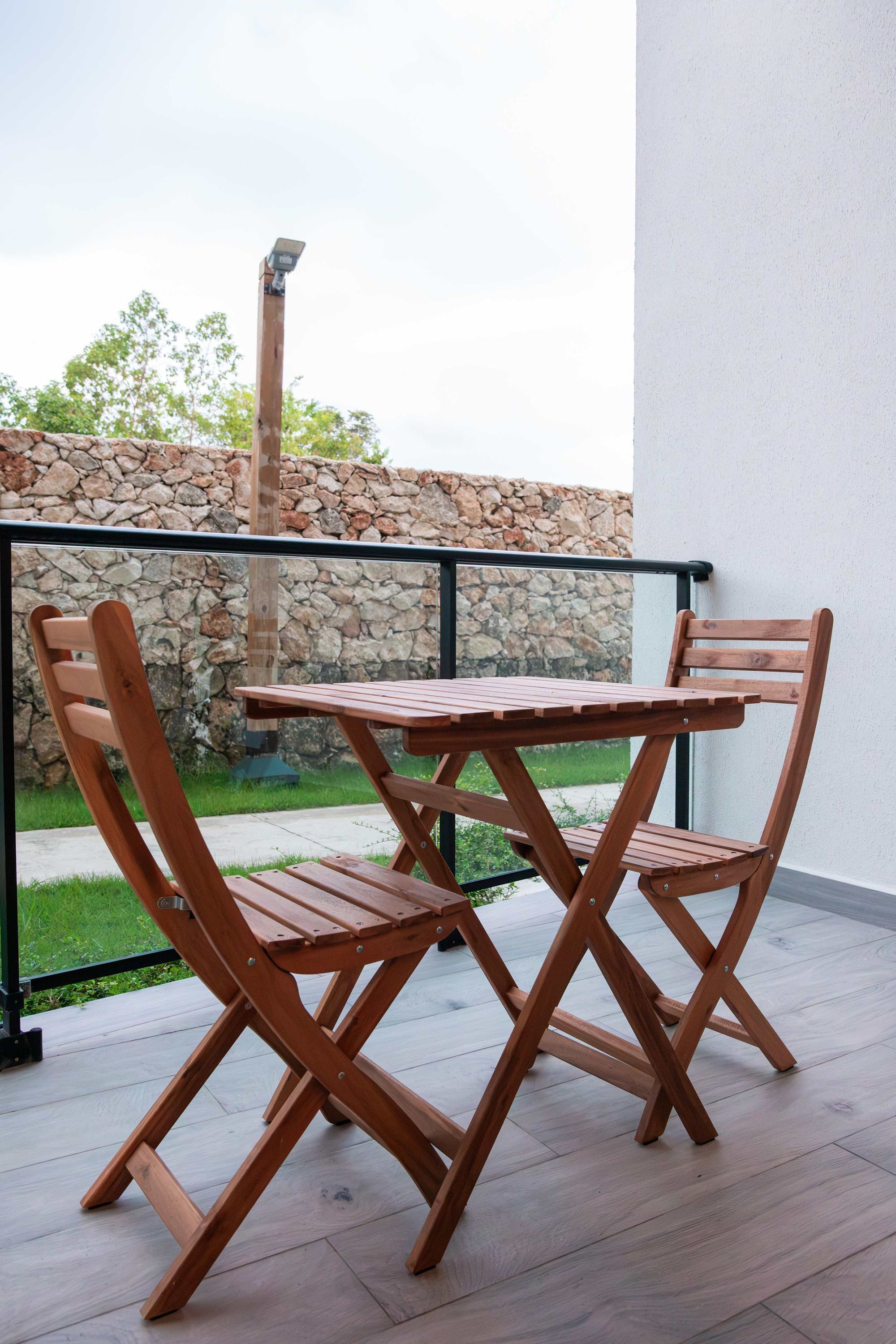 A wooden table and chairs on a balcony with a stone wall and a metal railing.