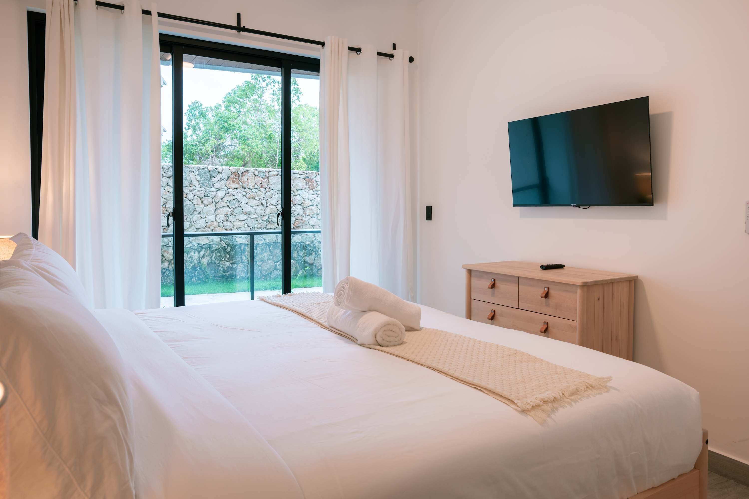 Un dormitorio con cama, televisor, cómoda de madera y balcón con pared de piedra.
