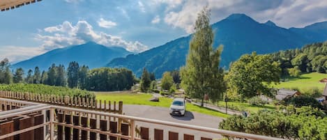 A balcony with a view of a mountain landscape, a road with a car, and a wooden fence.