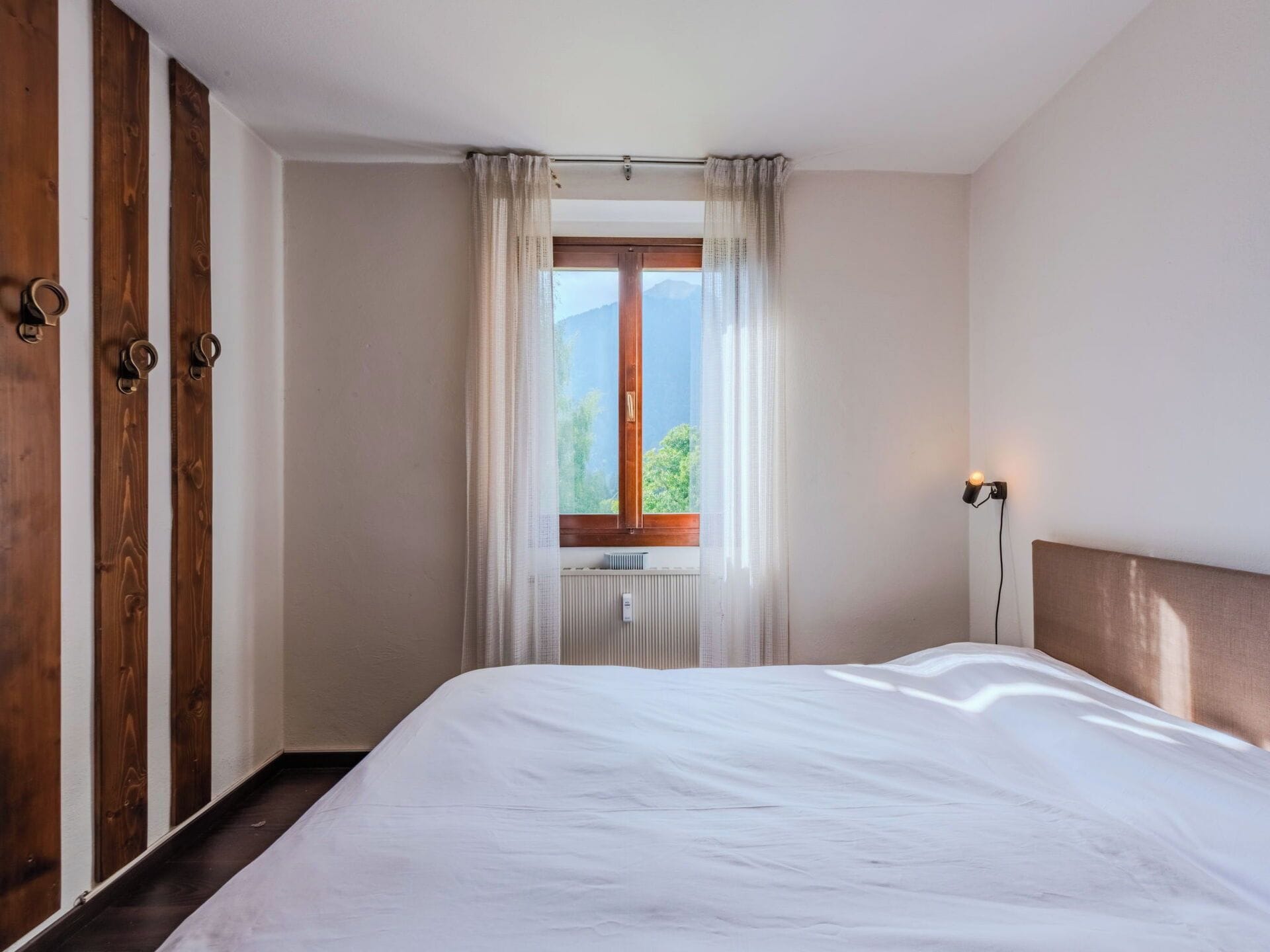 Ein Schlafzimmer mit einem großen Bett, einem Fenster mit Vorhängen, einem Holzschrank und einer Nachttischlampe.
