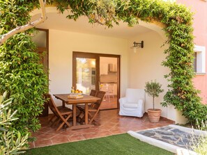 Eine Terrasse mit einem Holztisch und Stühlen, einem weißen Stuhl und einem kleinen Blumentopf.