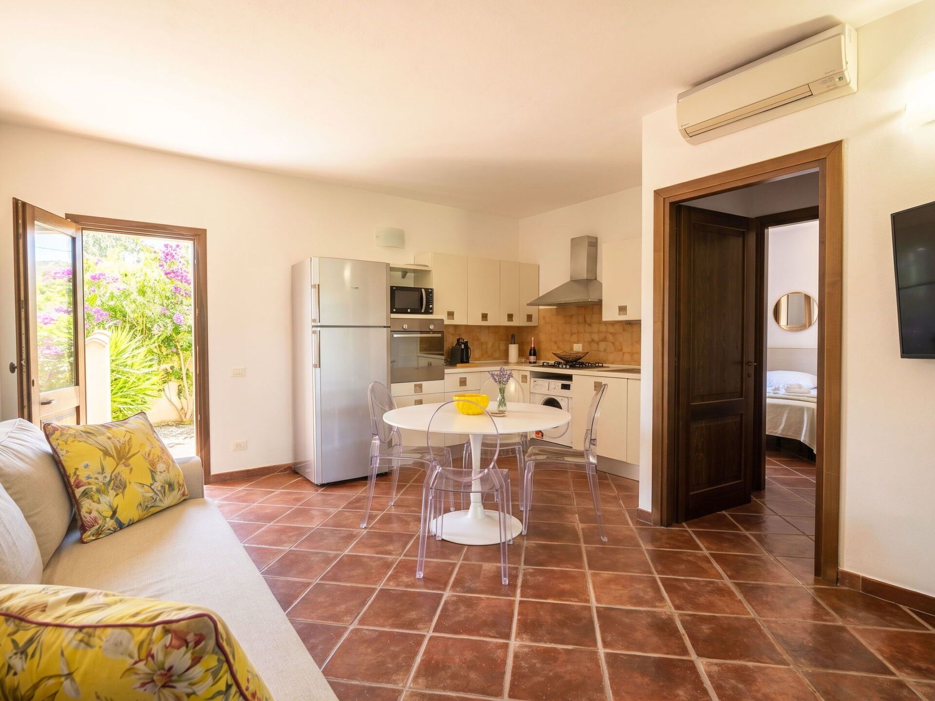 A compact kitchen with a refrigerator, microwave, and stove, a dining area with a table and chairs, and a living area with a sofa and a window.