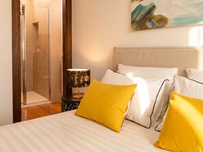 Quarto de hotel com cama, mesa de cabeceira, luminária e área de chuveiro.