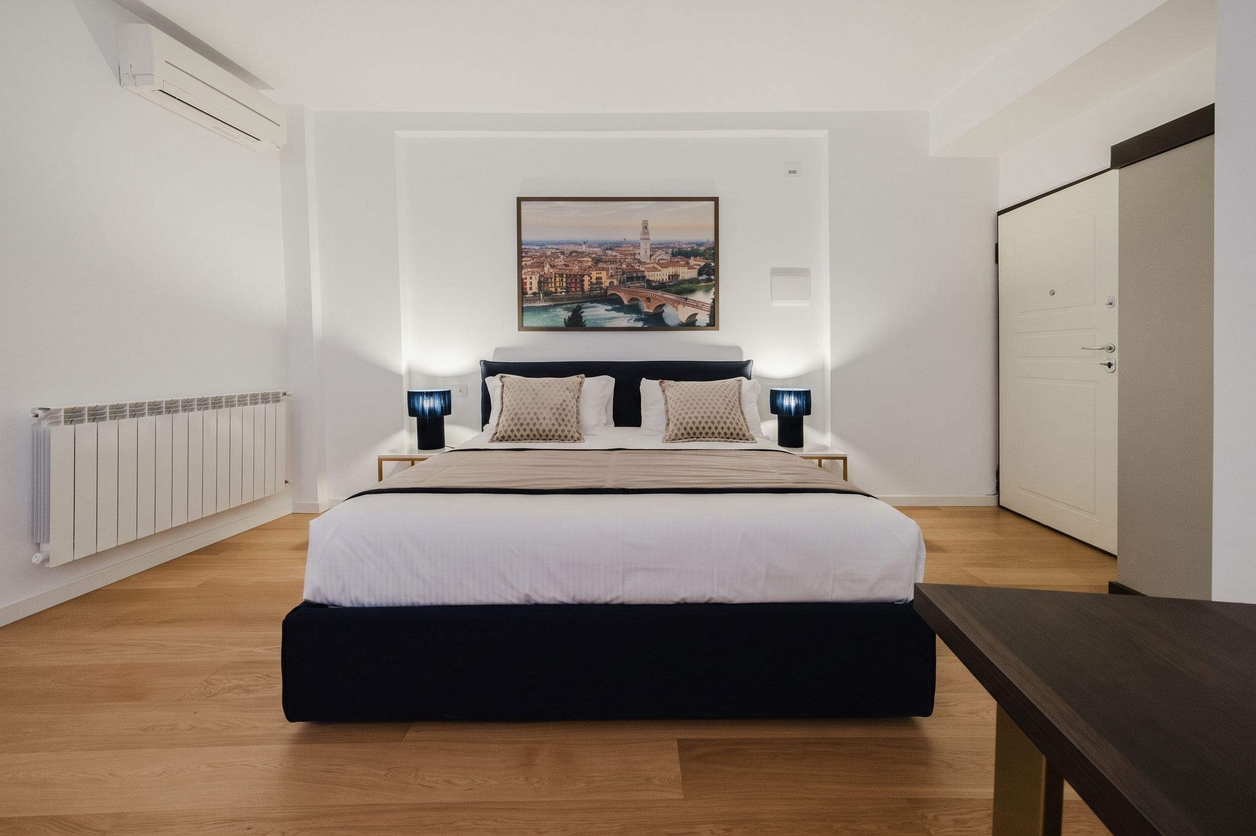 A modern bedroom with a large bed, a cityscape painting, and a wardrobe.