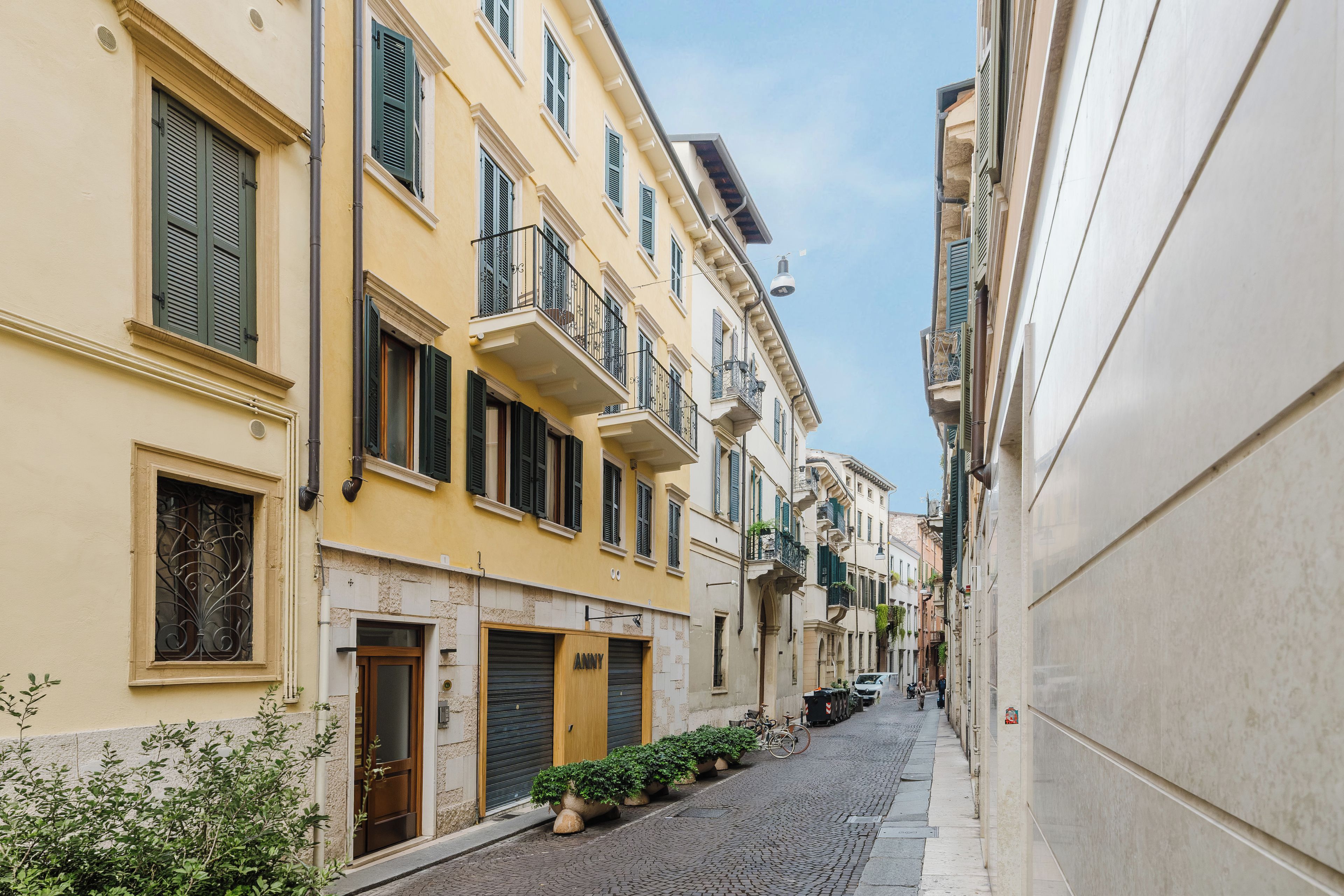 A narrow street with buildings on both sides, featuring balconies and shutters.