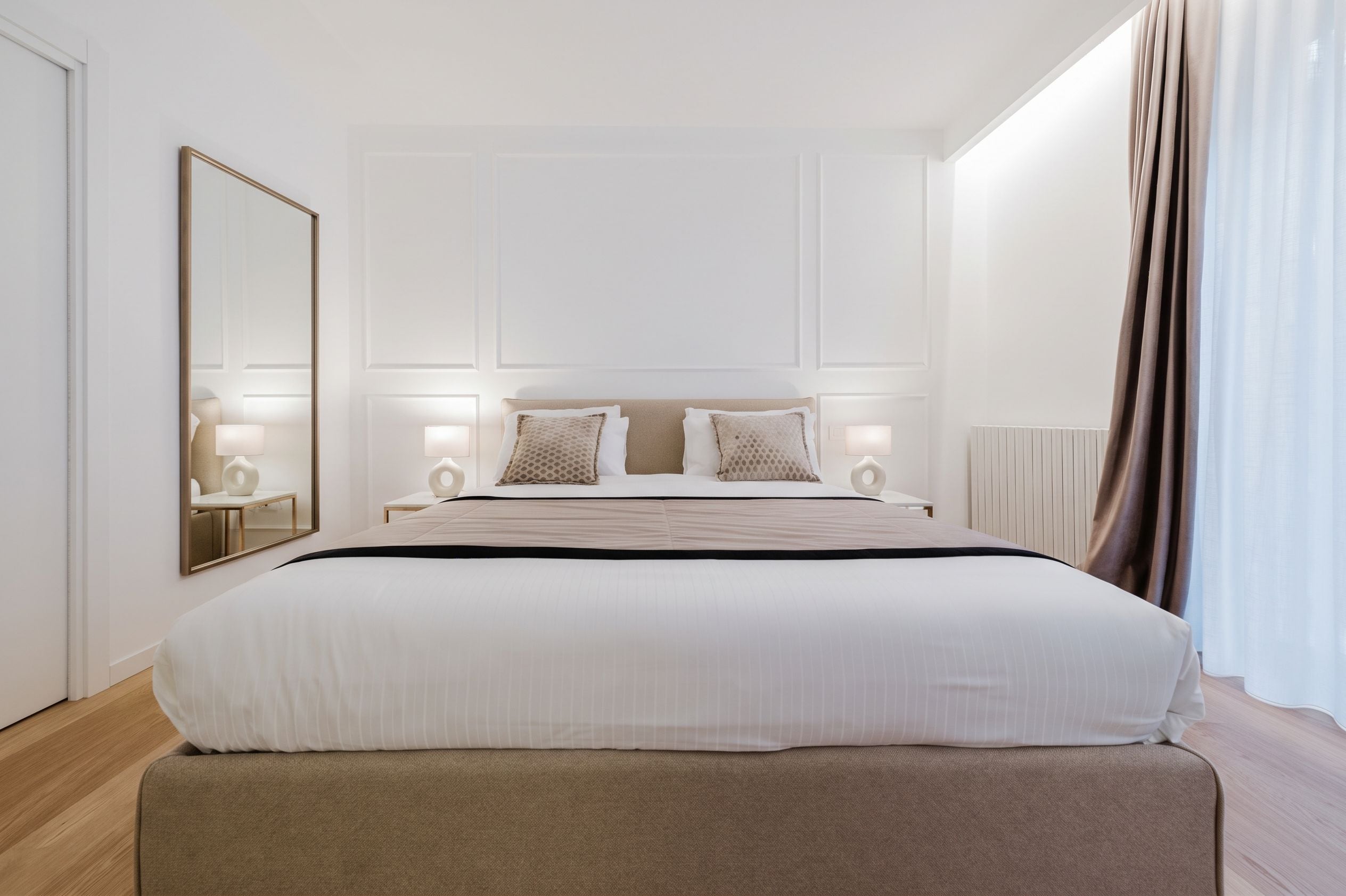 Una camera d'albergo con un letto grande, comodini, uno specchio e una finestra con tende.