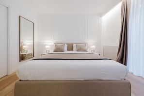 Ett hotellrum med en stor säng, sängbord, en spegel och ett fönster med gardiner.