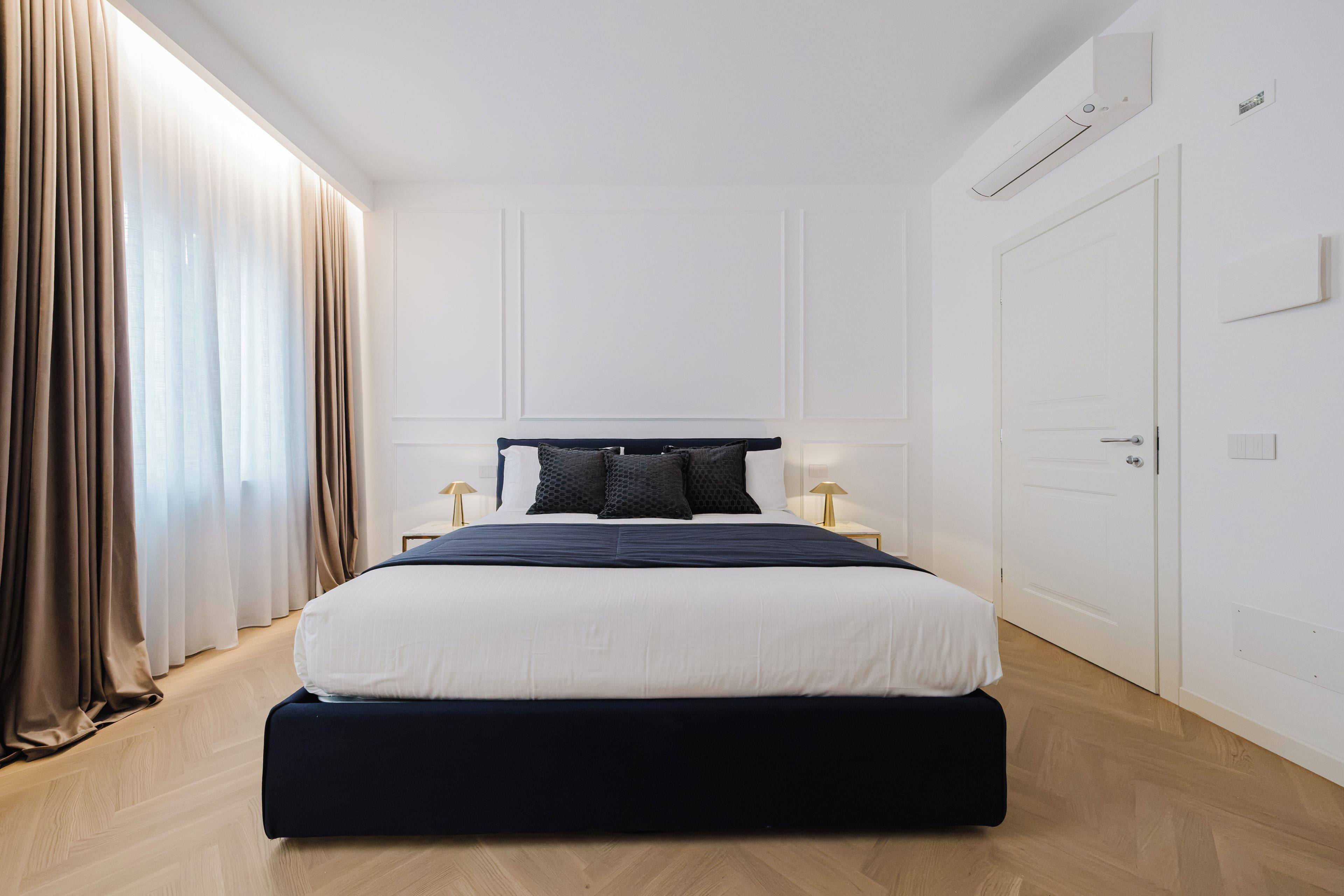 A modern hotel room with a large bed, a bedside table, a lamp, and a wardrobe.