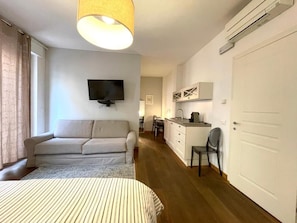 Un dormitorio con cama, sofá, televisión y una zona de kitchenette.