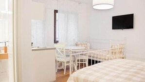 Une chambre à coucher comprenant un lit, une table de chevet, une chaise, une petite table et un téléviseur fixé au mur.